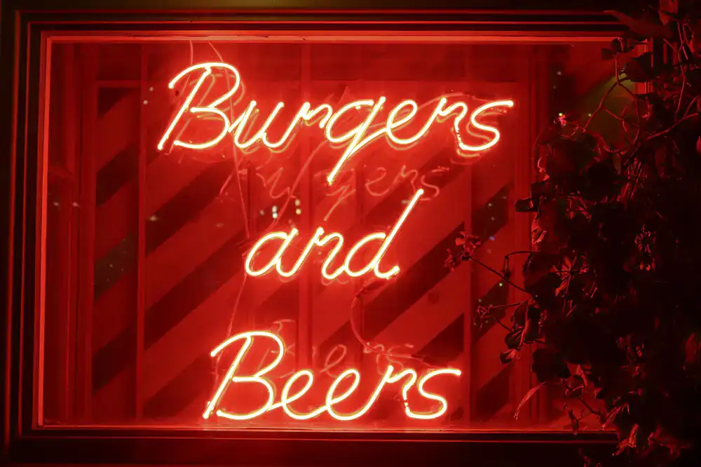A crafted burger and a cold pint of beer glowing under neon lights